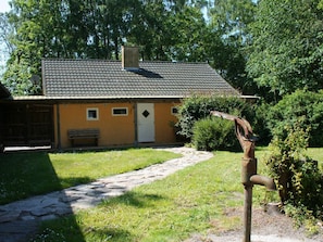 A rustic building with a tiled roof, a stone pathway leading to a wooden door, and a bench outside.