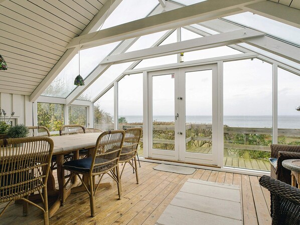A covered patio with a table and chairs, large windows, and a view of the sea.