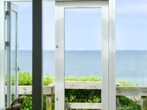 A view through a glass door to a wooden deck overlooking a calm body of water.