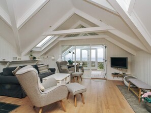 A loft-style room with a high ceiling, a large window, a flat-screen TV, and a dining area.