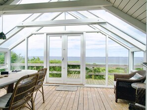 A covered deck with a table and chairs, large glass doors leading to a view of the sea.