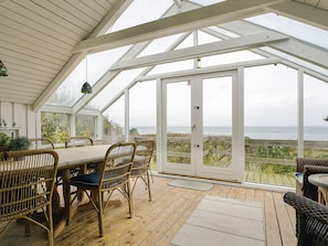 A covered patio with a table and chairs, large windows, and a view of the sea. - 5 Person Holiday Home in Asnaes-by Traum (Asnaes)