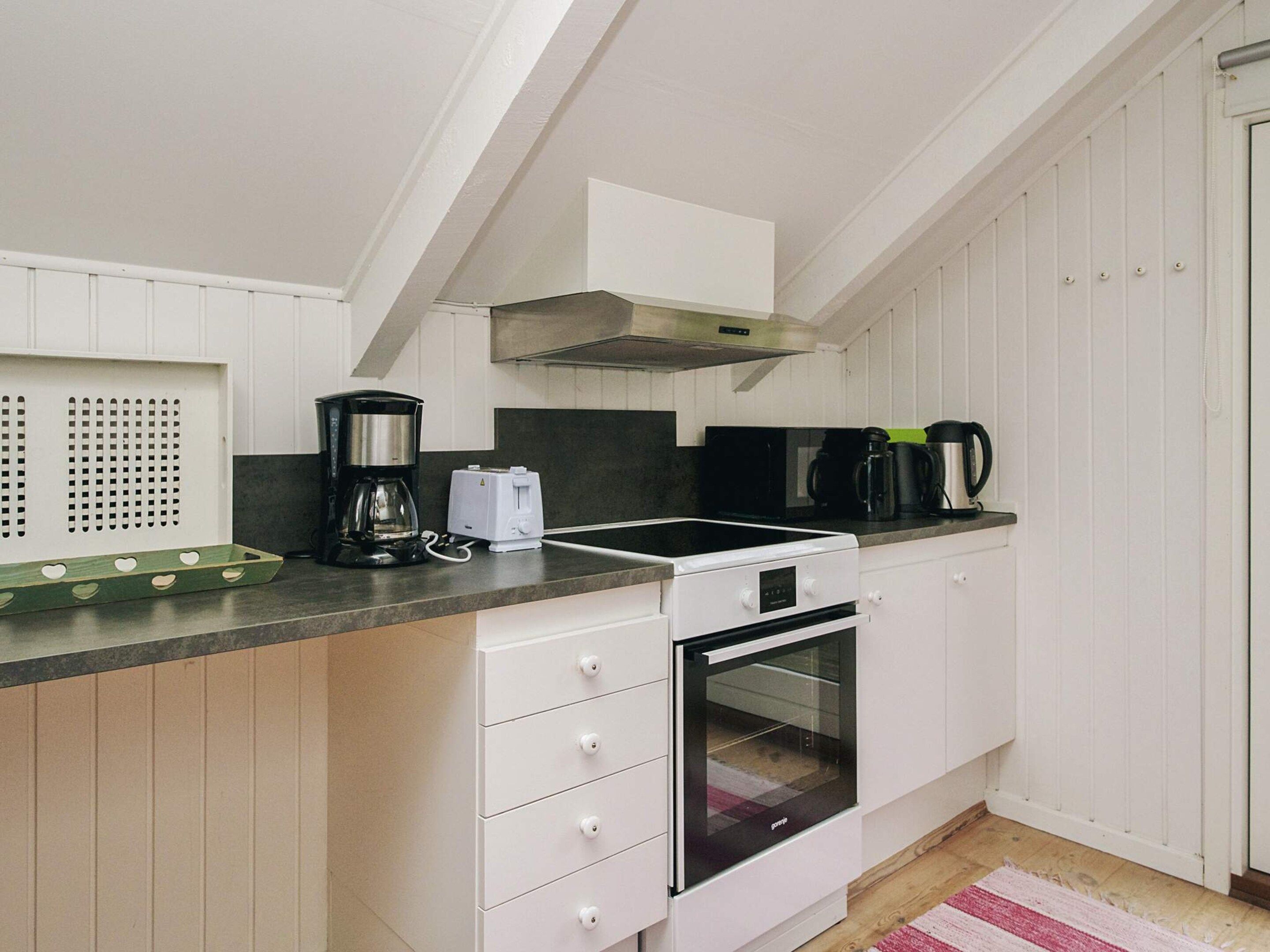 Une cuisine avec des meubles blancs, une cuisinière noire, une machine à café et un grille-pain.