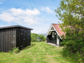 Et sort metalskur med nummer 12, en lille træbygning med rødt tag, og et græsareal med træer.