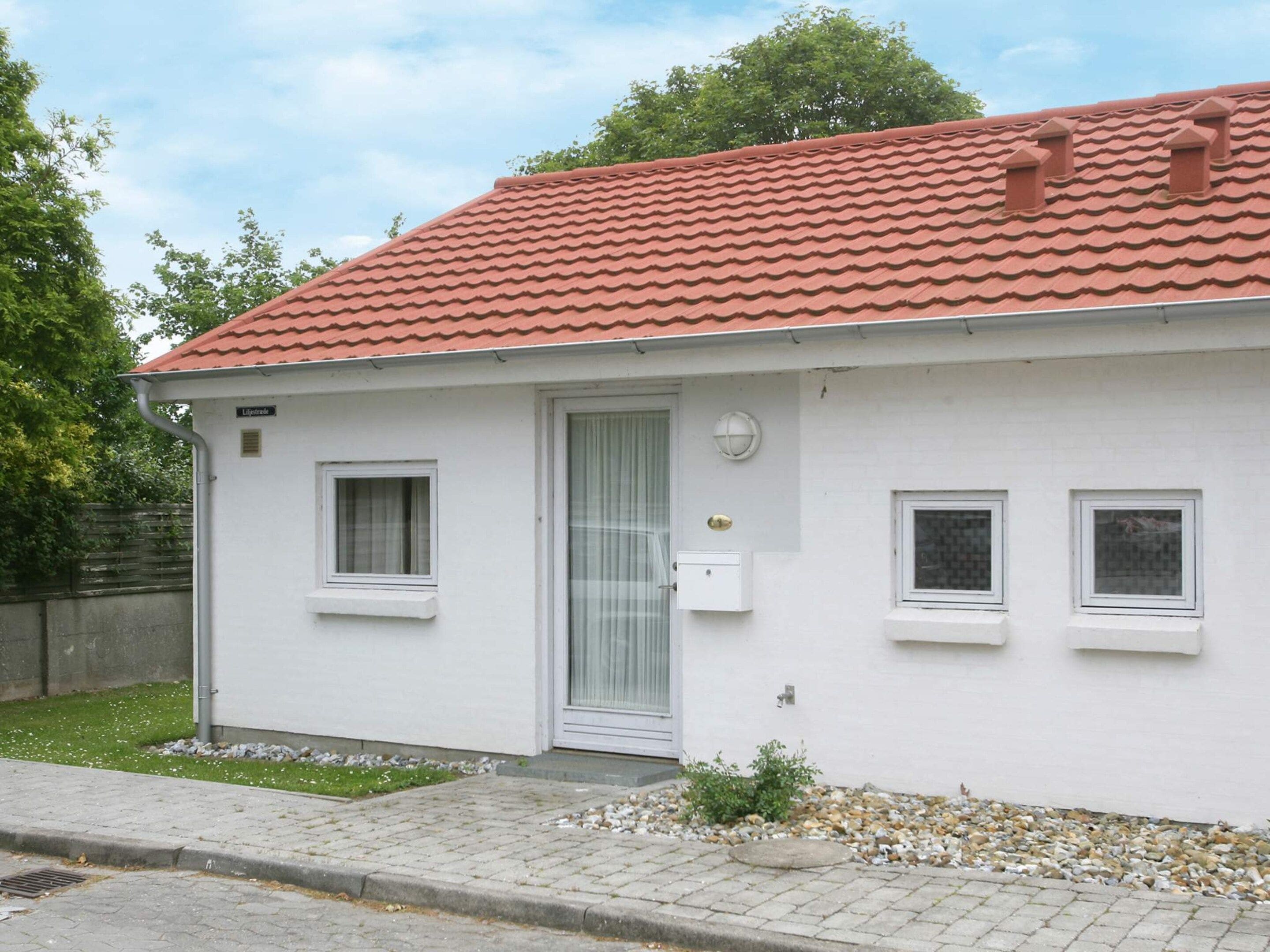A single-story building with a red-tiled roof, a white exterior, and a small front porch with a door and windows.