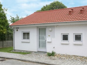 Una edificación de un piso con techo de tejas rojas, fachada blanca y un pequeño porche con puerta y ventanas.