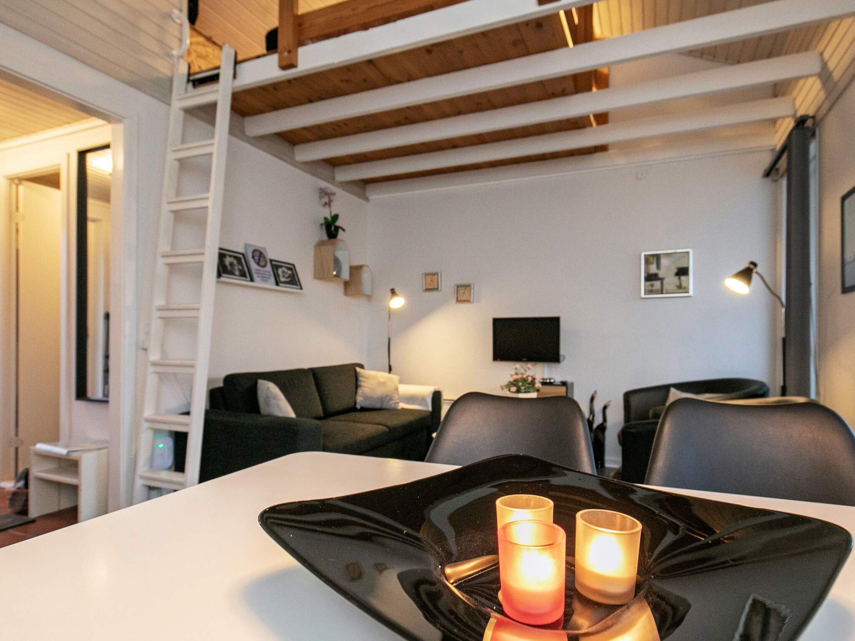A modern living room with a white sofa, a black dining table with candles, and a TV on the wall.