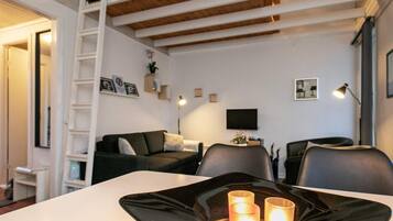A modern living room with a white sofa, a black dining table with candles, and a TV on the wall.