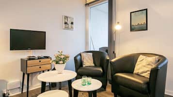 A modern living room with a flat-screen TV, a sofa, a coffee table, and a small side table with a vase of flowers.