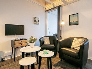 A modern living room with a flat-screen TV, a sofa, a coffee table, and a small side table with a vase of flowers. - Cozy Holiday Home in Ã†rÃ¸skÃ¸bing near Harbour (Aeroskobing)