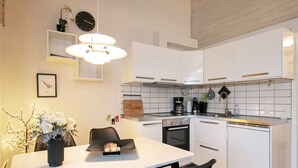 A modern kitchen with white cabinets, a dining table with chairs, a hanging light fixture, a clock, and a small plant on the wall. - Cozy Holiday Home in Ærøskøbing near Harbour (Aeroskobing)