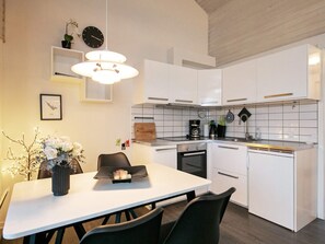 A modern kitchen with white cabinets, a dining table with chairs, a hanging light fixture, a clock, and a small plant on the wall. - Cozy Holiday Home in Ã†rÃ¸skÃ¸bing near Harbour (Aeroskobing)