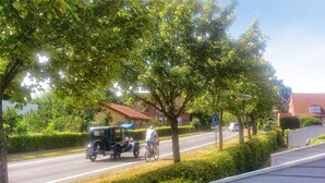 A street scene with a vintage car, a cyclist, and a residential area with houses and greenery.