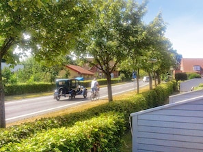 A street scene with a vintage car, a cyclist, and a residential area with houses and greenery.