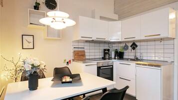 A modern kitchen with white cabinetry, a dining table with chairs, a hanging light fixture, and a clock on the wall.