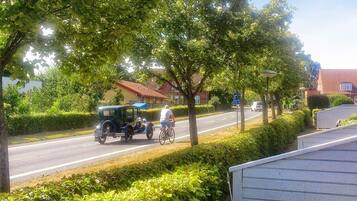 A street scene with a vintage car, a cyclist, and a residential area with houses and greenery.
