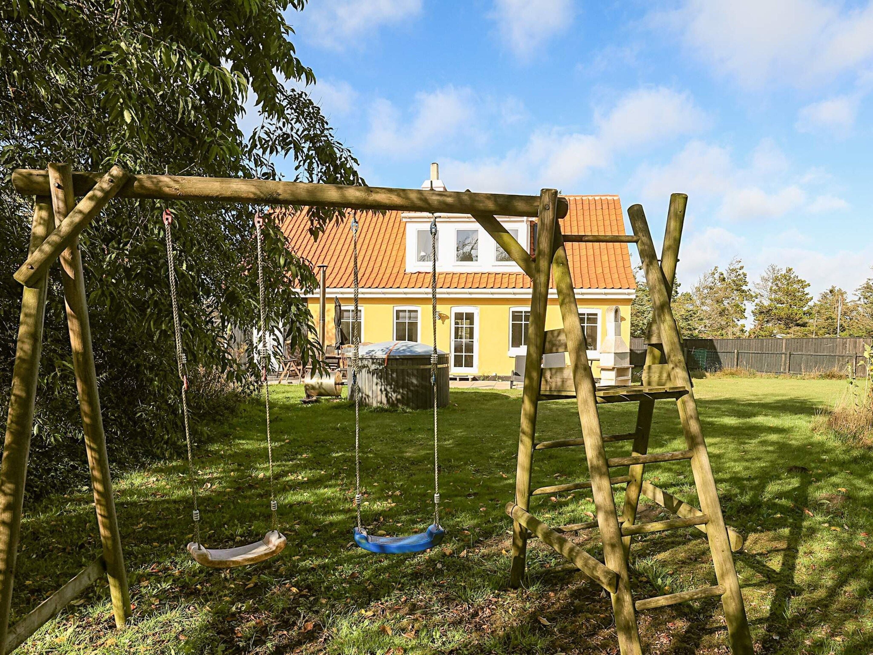 A wooden swing set in a yard with a yellow house in the background.