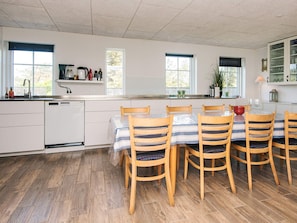 Une cuisine moderne avec un coin repas, comprenant une table à manger en bois avec des chaises, un lave-vaisselle encastré et une fenêtre donnant sur l’extérieur.