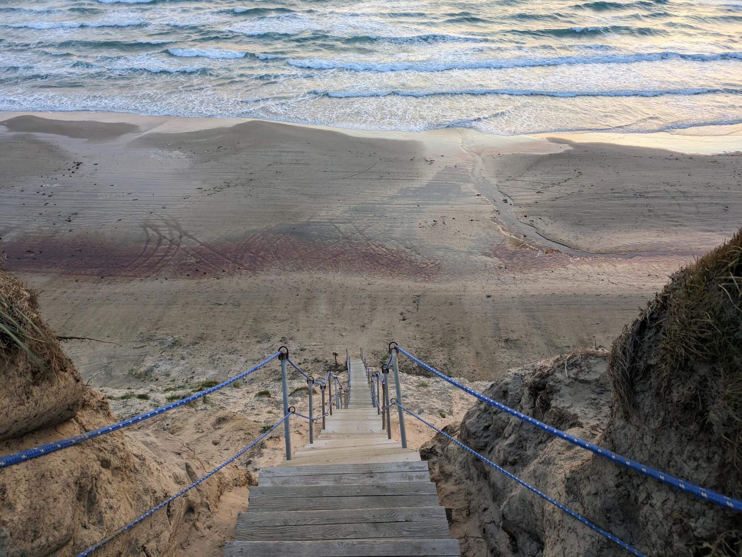 A wooden staircase leading to a beach with a sandy shore and ocean waves.