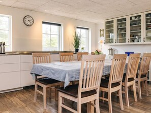 A dining area with a table set for six, wooden chairs, a clock on the wall, and a cabinet with dishes.