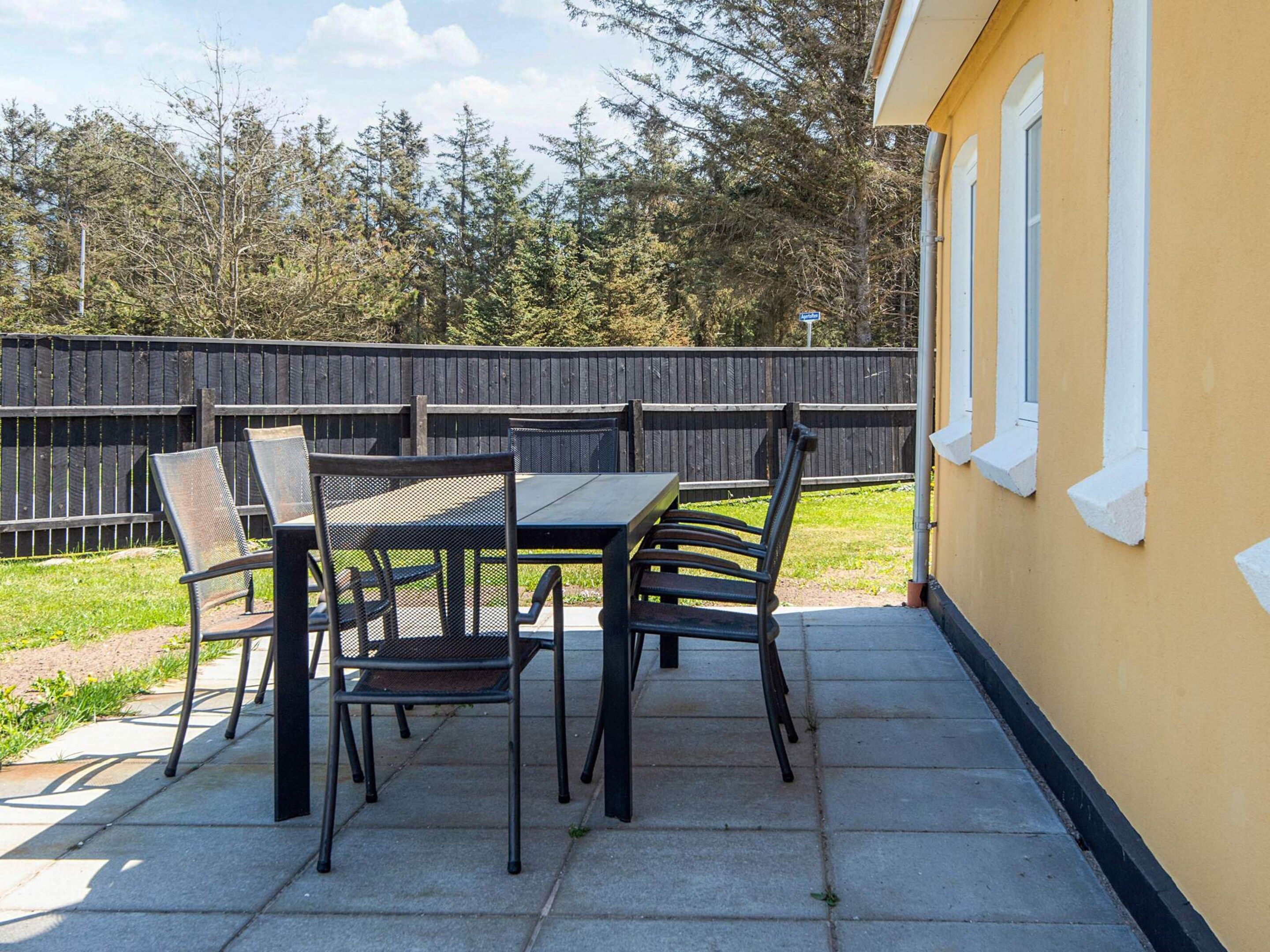 Un patio al aire libre con una mesa y sillas, una cerca de madera y un muro amarillo.