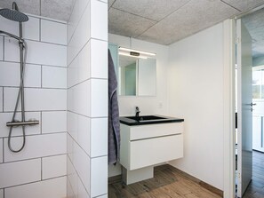 Une salle de bain moderne avec des murs carrelés de blanc, un plancher en bois, un lavabo noir et une douche équipée d’un pommeau de douche à main.