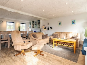 Uma sala de estar ampla com sofá, poltronas, mesa de centro e canto de jantar com mesa e cadeiras.