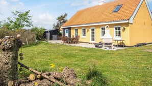 A yellow house with a tiled roof, a patio with a table and chairs, and a chimney. - 4 Star Holiday Home in Lokken (Lokken)