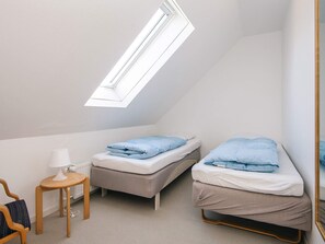 A small, well-lit room with two beds, a table, and a chair.