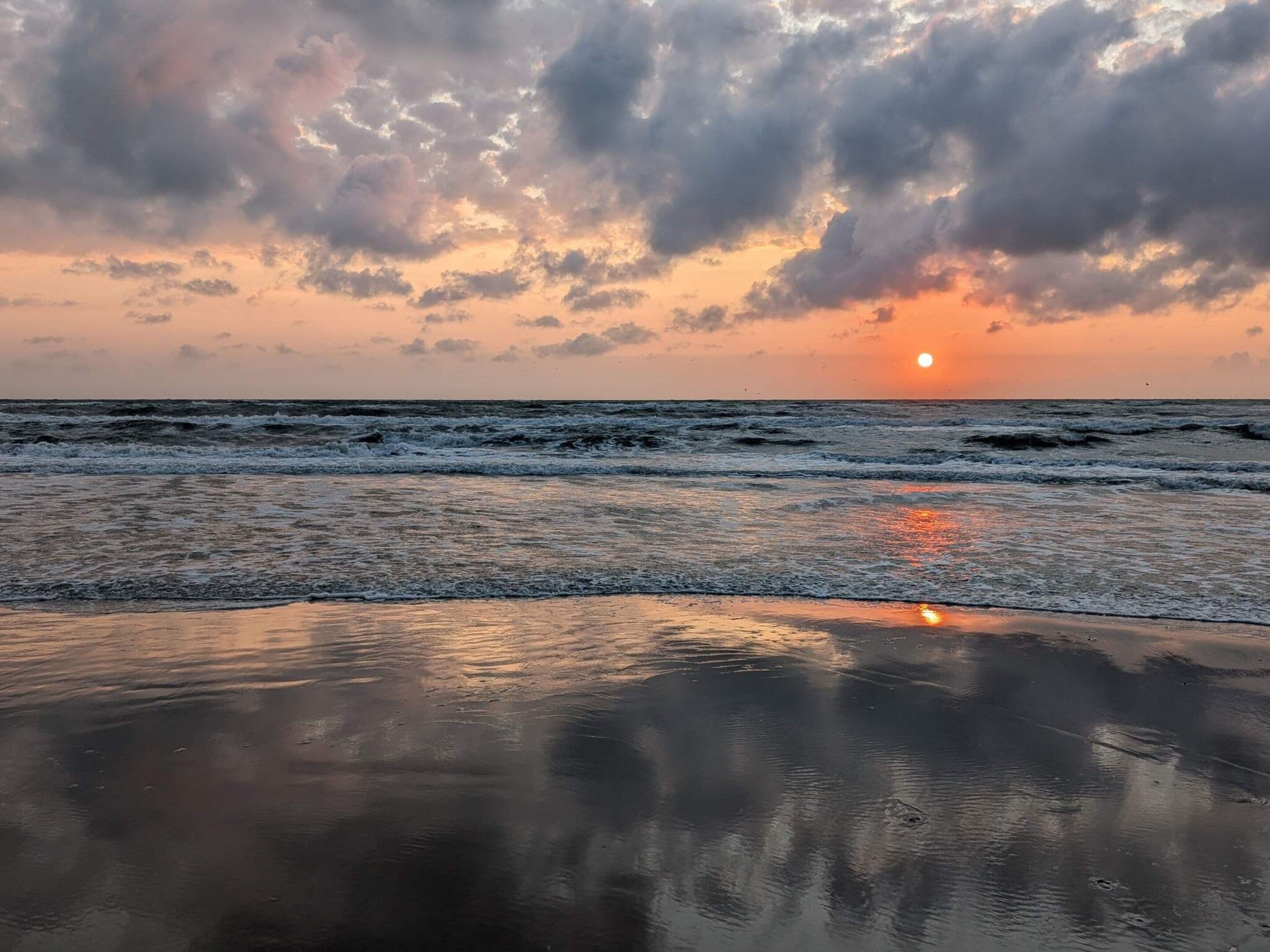 Une plage avec des vagues, un coucher de soleil et un ciel nuageux.
