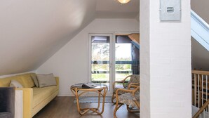 A cozy room with a yellow sofa, a small table, and two wicker chairs. There's a sliding glass door leading to an outdoor area. - 4 Star Holiday Home in Lokken (Lokken)