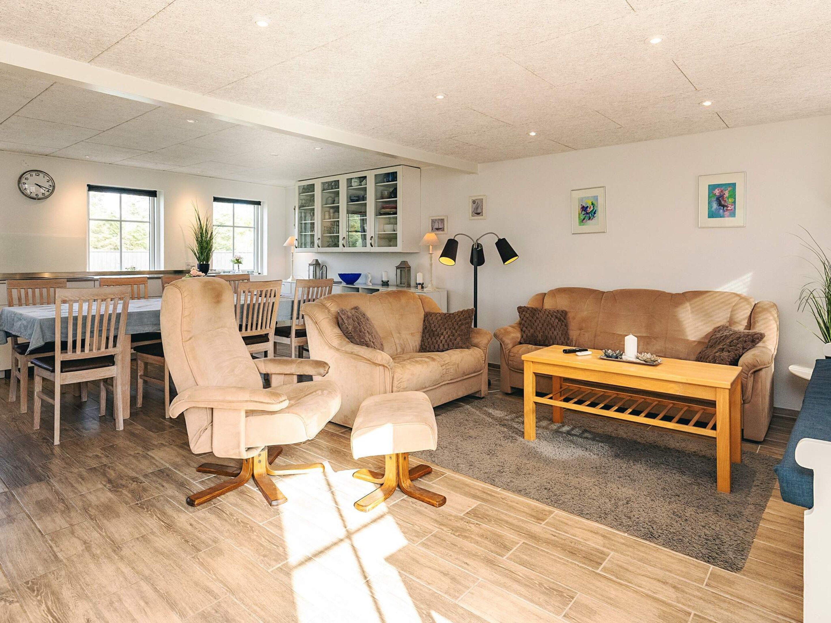A spacious living room with a dining area, wooden flooring, and a kitchen in the background.