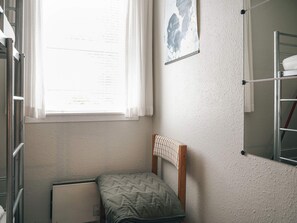 Una habitación pequeña y compacta con una cama litera, una ventana con cortinas, una pizarra y un estante metálico.