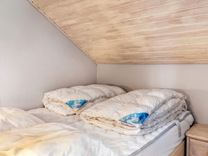 A single bed with a wooden headboard, a nightstand, and a wall with a sloped ceiling.