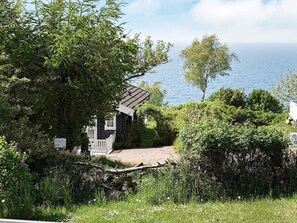 Una cabaña pequeña con un muelle de madera, rodeada de abundante vegetación y con vista a un cuerpo de agua.