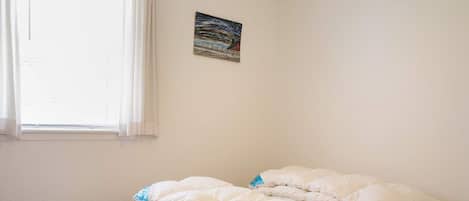 Un dormitorio con cama, ventana con cortinas y un cuadro en la pared.