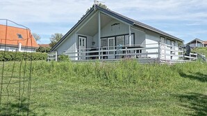 A white building with a sloped roof, a balcony, and a fenced area with grass and flowers. - 6 Person Holiday Home in Hasle (Hasle)