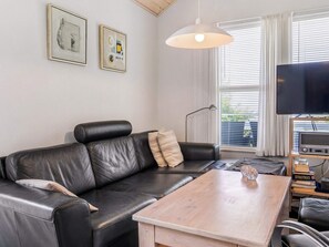 Un salon avec un canapé en cuir noir, une table basse en bois, un téléviseur et une bibliothèque remplie de livres.
