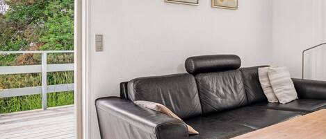 Ein modernes Wohnzimmer mit einem schwarzen Ledersofa, einem Holztisch und zwei gerahmten Kunstwerken an der Wand.