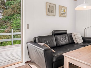 A modern living room with a black leather sofa, a wooden table, and two framed artworks on the wall.