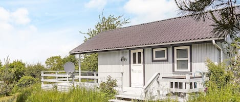 A single-story house with a grey roof and white exterior, a front porch, and a satellite dish.