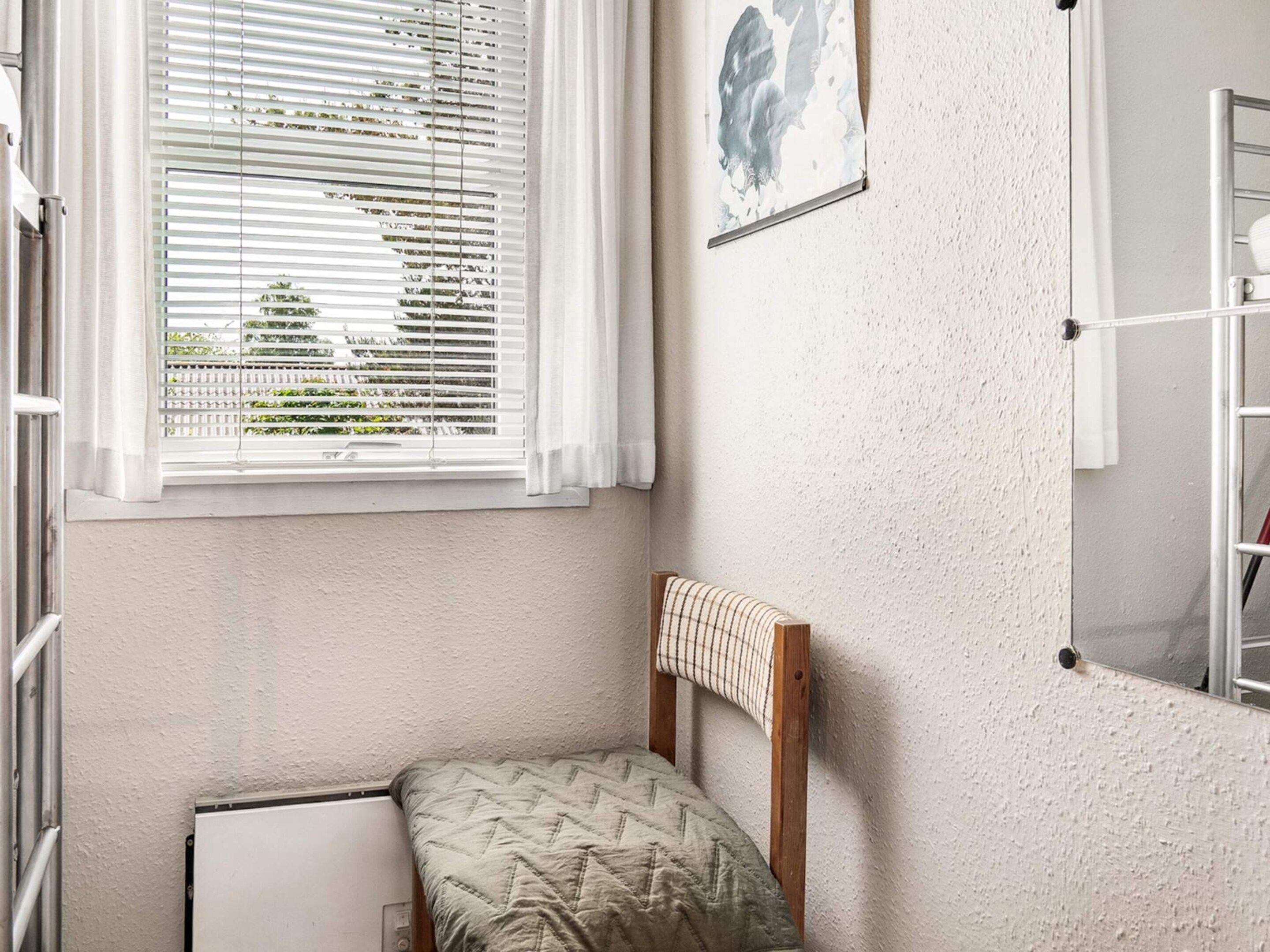 A small, single-bed room with a window, a radiator, and a wall-mounted shelf.