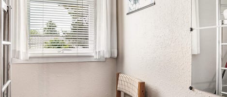 A small, single-bed room with a window, a radiator, and a wall-mounted shelf.