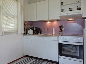 Una cocina compacta con armarios blancos, una estufa y un microondas.