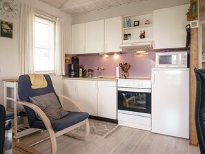 A compact kitchen with white cabinets, a microwave, a stove, and a chair. - 6 Person Holiday Home in Hasle (Hasle)