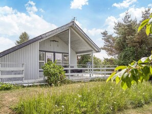 A single-story building with a covered porch, a satellite dish, and a small garden area. - 6 Person Holiday Home in Hasle (Hasle)