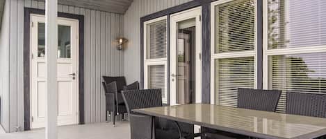 A covered patio with a table and chairs, a door, and windows with blinds.