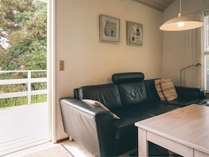 A room with a black leather sofa, a wooden table, and two framed artworks on the wall.