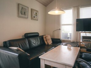 A living room with a black leather sofa, a wooden coffee table, a floor lamp, a flat-screen TV, and framed artwork on the wall. - 6 Person Holiday Home in Hasle (Hasle)