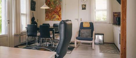 A dining area with a table, chairs, a painting, and a clock on the wall.